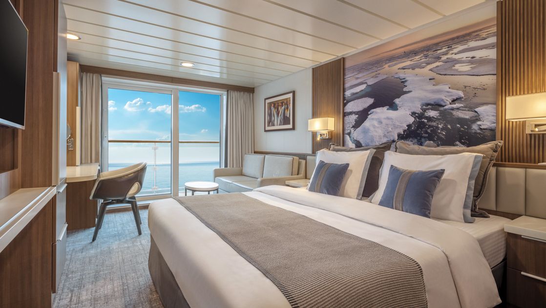 Cat B Balcony Stateroom on Sylvia Earle ship with king bed & iceberg photo behind, tv, wood accents & glass door to balcony.