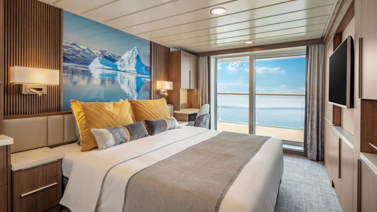 Junior Suite on Sylvia Earle ship with king bed & iceberg photo behind, tv, wood accents & sliding glass door to balcony.
