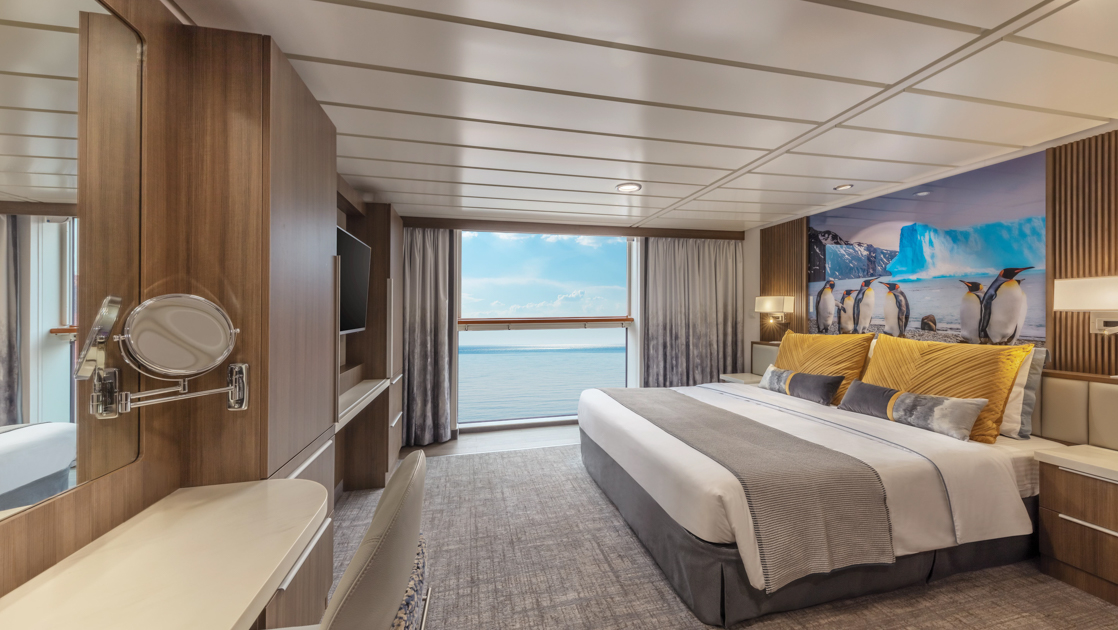 Superior Stateroom on Sylvia Earle ship with king bed & penguins photo behind, tv, wood accents & large glass view window.