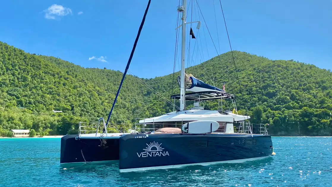 Belize catamaran Ventana al Mar with dark blue hulls & white upper deck sits in turquoise water in sun by bright green island
