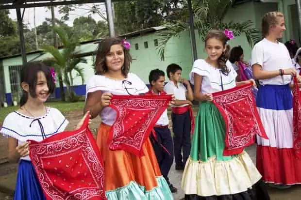 Young Costa Rican girls in colorful dresses with young boys behind them at a local school.