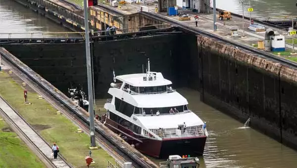 Small red-&-white ship travels through the Panama Canal on a cruise.