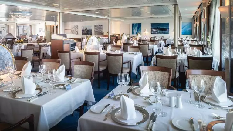 Dining room with 4-top tables set for formal dinner service aboard Antarctica ship Seaventure.