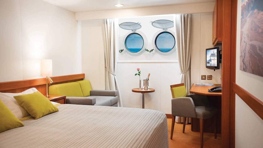 Porthole Stateroom on Seaventure expedition ship, with queen bed, desk, chair, TV & 2 portholes.