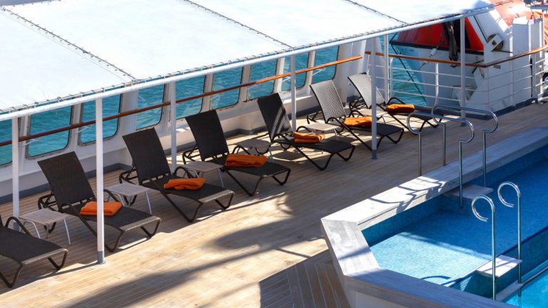 Heated saltwater pool with covered, wind-protected chaise loungers on top deck of M/S Seaventure ship.