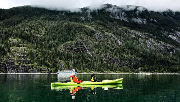 Two guests enjoy a kayaking activity inside the waters of Endicott Arm, an experience to remember after combining their Alaska land tour with a cruise.