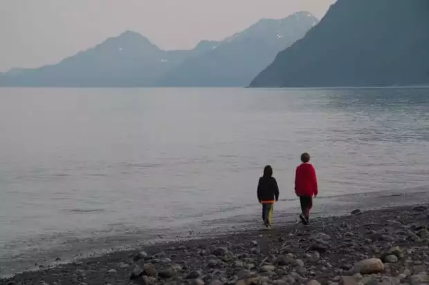 Two young boys walking along a beach in Alaska with mountains in the background.