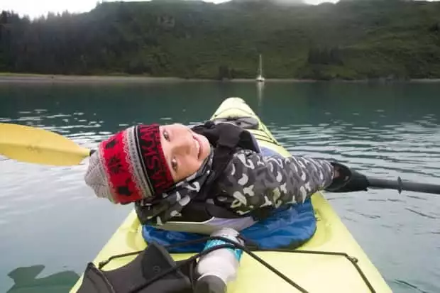 One kid in the front of a yellow kayak laying back and looking back while kayaking through Alaska.