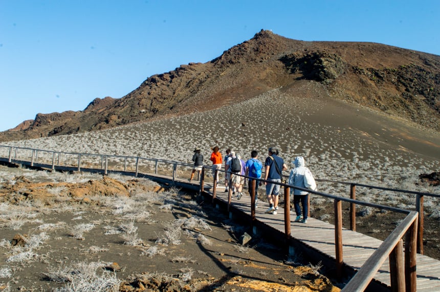 A shore excursion on a Camila Galpagos cruise a group of travelers walk on a wooden path up the desert like lava side of Bartolome Island to the top view point.