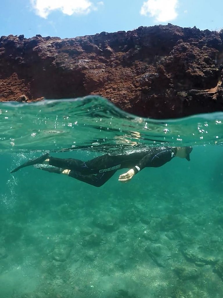an underwater photo of a snorkeler, outfitted in a long wet suit, fins, mask and snorkel, swims in the ocean as an activity on a Camila Galapagos cruise