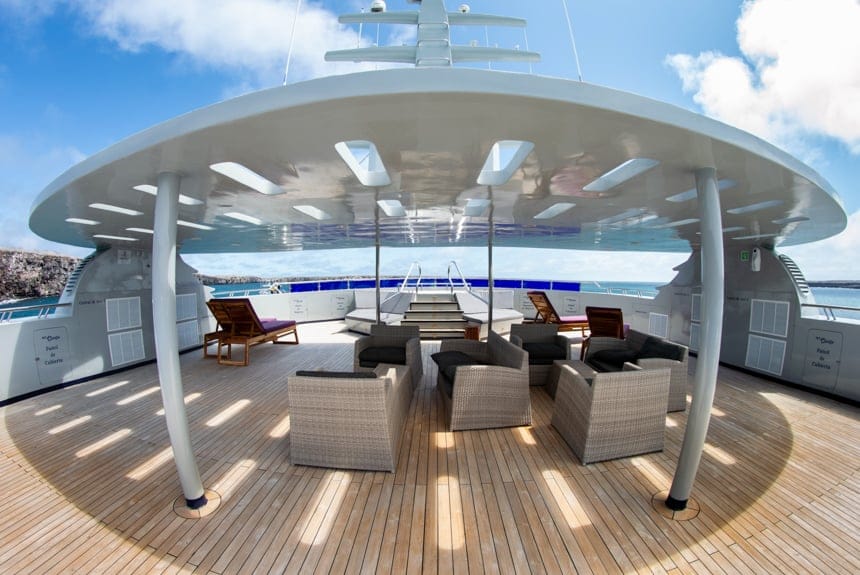 The sun deck aboard Camila Galapagos trimaran, a shade cover stands above a seating area in front of a jacuzzi with a panoramic view
