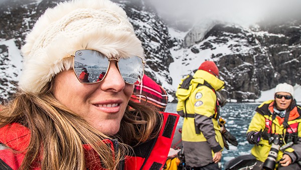 Close-up of a female traveler in sunglasses, white fur hat and red jacket on an Antarctica cruise with two fellow passengers