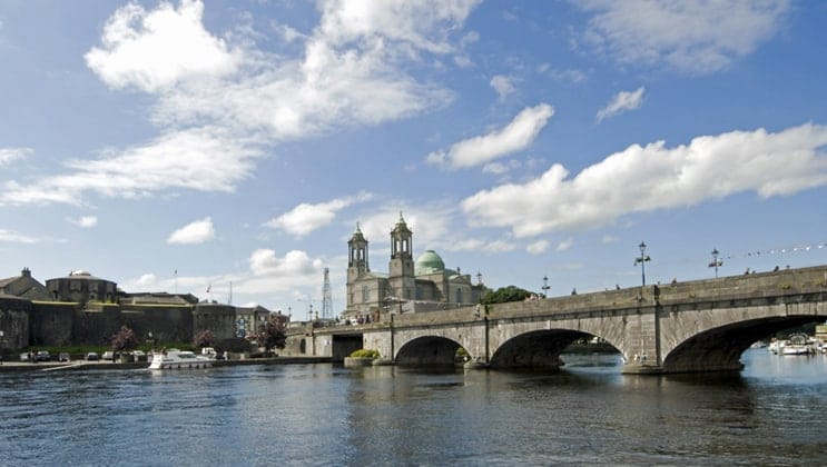 Calm, wide River Shannon running under the large stone bridge at Athlone under a sunny sky during an Ireland barge cruise.