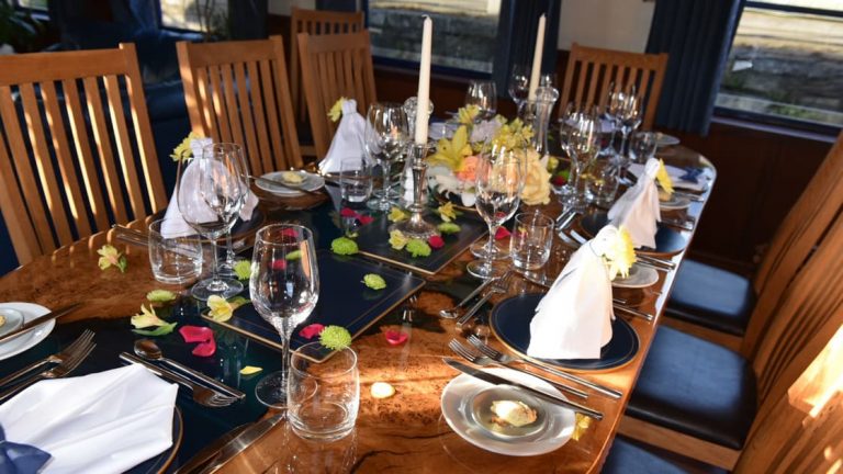 10-guest dining table set for dinner with white linens, candles, flowers & wine glasses aboard River Thames barge Magna Carta.