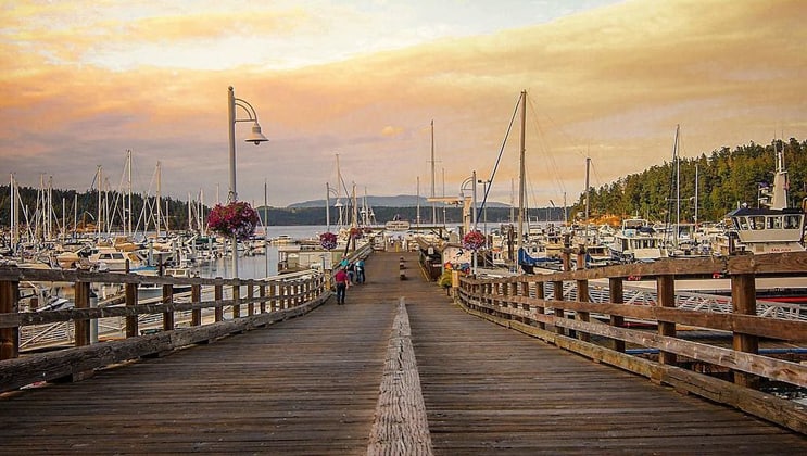 Long wooden wharf leading down to docks with small private boats in Friday Harbor, Washington, at sunset.