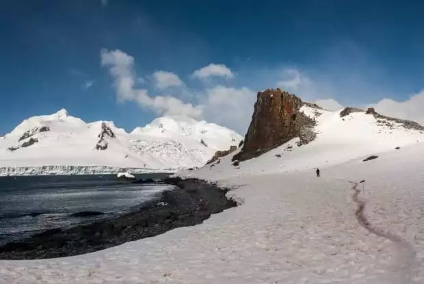 Person hiking in the snow along the ocean in Antarctica. 