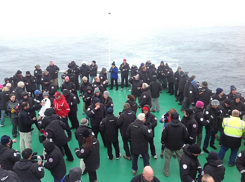 Guests aboard a small ship cruise on the deck together in Antarctica. 