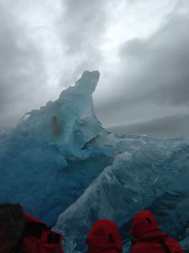 Small ship cruise guests up close to blue iceberg in the Arctic. 