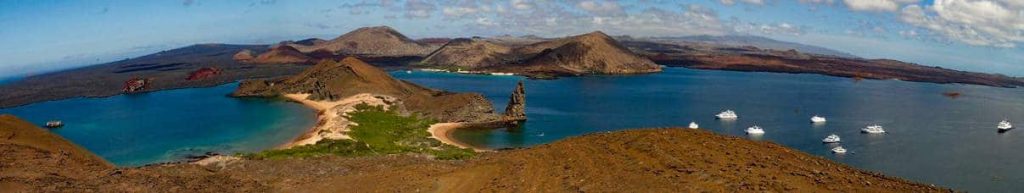 on a clear blue sky day a panoramic view from the top of Bartolome Island 7 small boats float in the water around the famous Pinnacle Rock