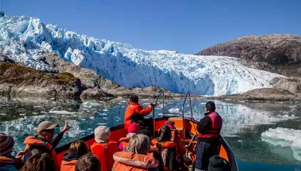 Travelers in a small orange boat approach a blue-white glacier on a Patagonia cruise.