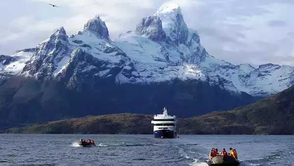 Patagonia Australis cruise ship with mountains in the background and two skiffs heading toward the camera.