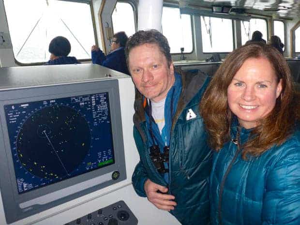 Two guests smiling by the navigation map on the bridge of  a small ship cruise in Antarctica. 