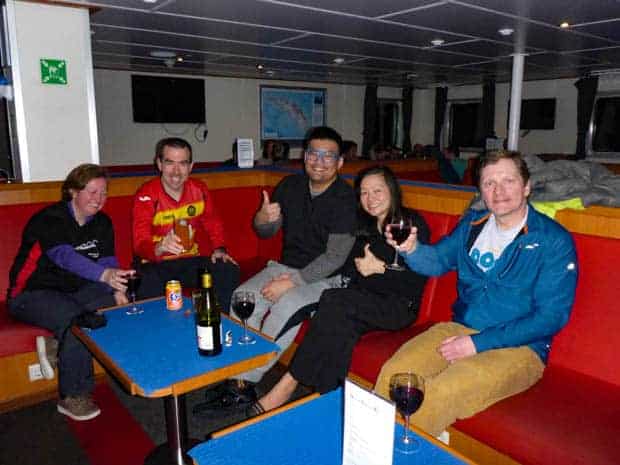Guests aboard a small ship cruise in Antarctica drinking wine together and giving a thumbs up. 