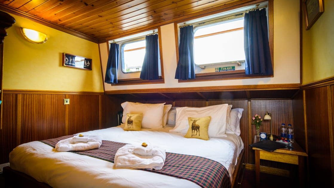 Warmly lit below-deck stateroom with double bed, wooden furniture & 2 windows aboard Scottish Highlander Scotland barge.