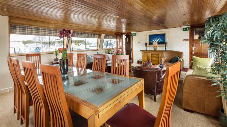 Dining table & saloon area with couches, chairs & coffee tables aboard Shannon Princess barge.