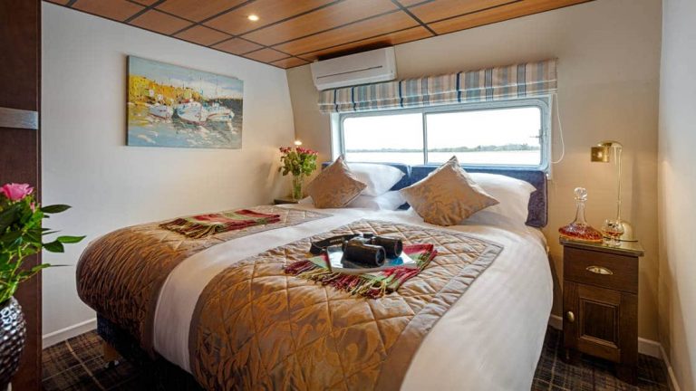 Suite aboard Shannon Princess barge with double bed, white-&-gold linens, large view window, 2 bedside tables & binoculars.
