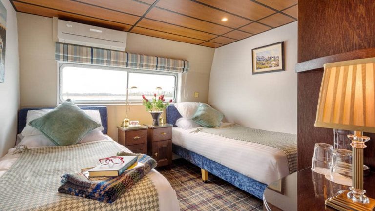 Suite aboard Shannon Princess barge with 2 twin beds, beige linens, large view window, bedside table & binoculars.
