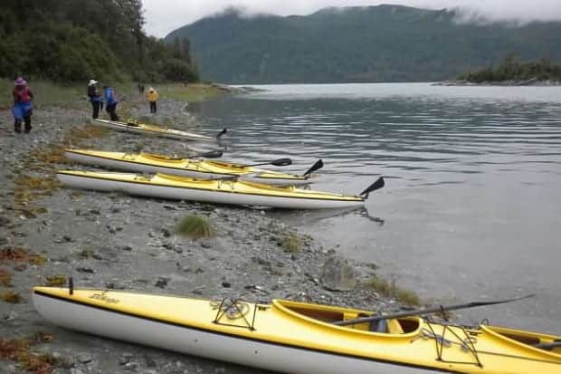 4 yellow kayaks pulled up on beack with small ship cruise travelers milling about the shoreline.