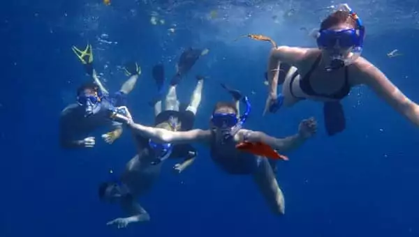 Group of 5 snorkelers in deep blue water with dark blue masks & snorkels & black fins during a Belize family vacation.