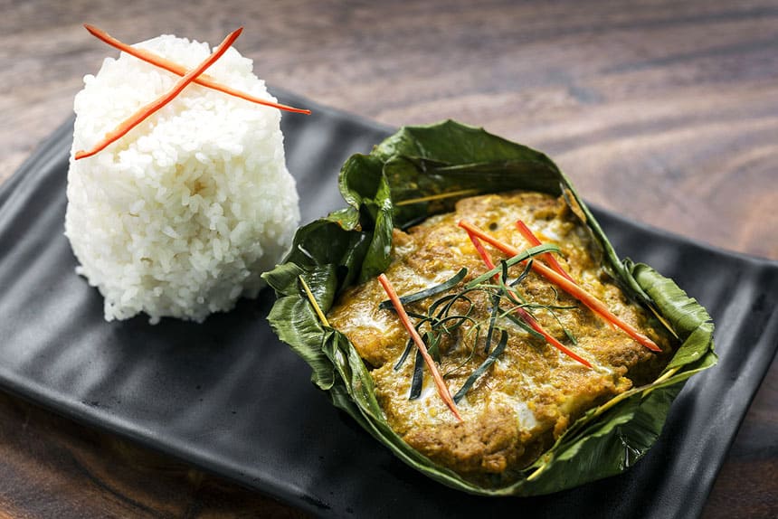 Chef David Thompson's Fish Amok Snakehead Curry presented in a green leaf with a cake of rice beside it on a black plate, offered during Aqua Mekong River Cruises.