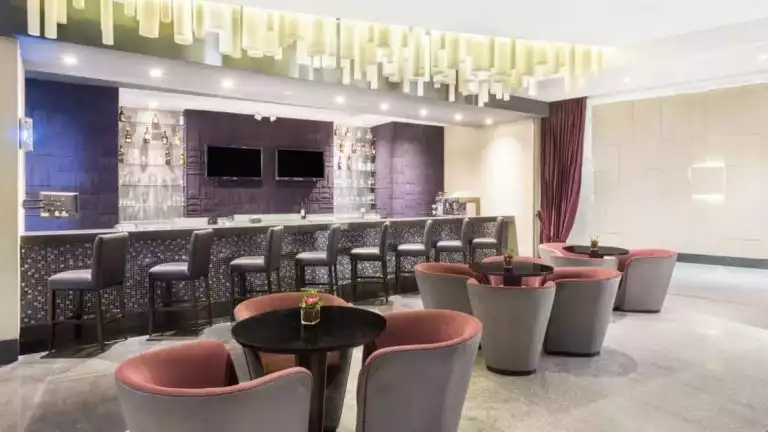 Numa lobby bar at Wyndham Guayaquil Hotel, with soft velvet chairs in trios, long bar with modern tall chairs & cylindrical lights above the bar.