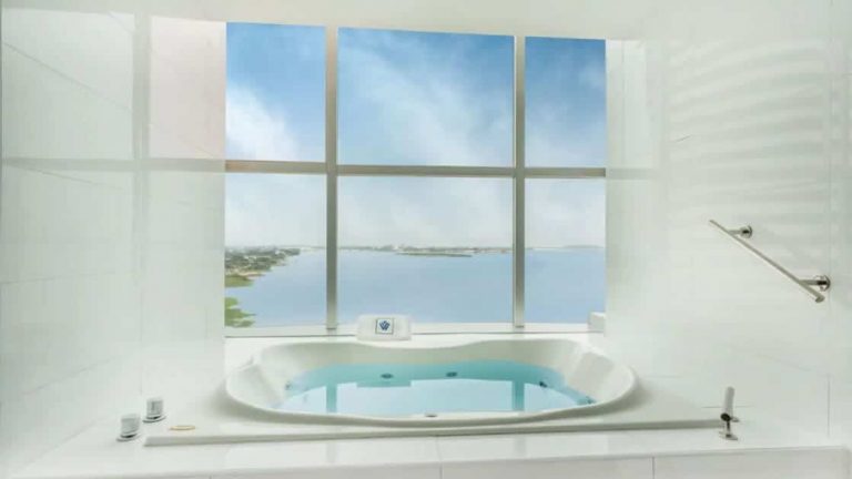 Presidential Suite white Jacuzzi with large windows looking out onto a sunny day & ocean at Wyndham Guayaquil Hotel.