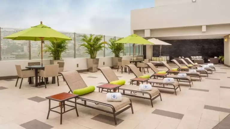 Rooftop terrace with chaise loungers & tables with chairs & lime green umbrellas on a sunny day at the Wyndham Guayaquil Hotel.