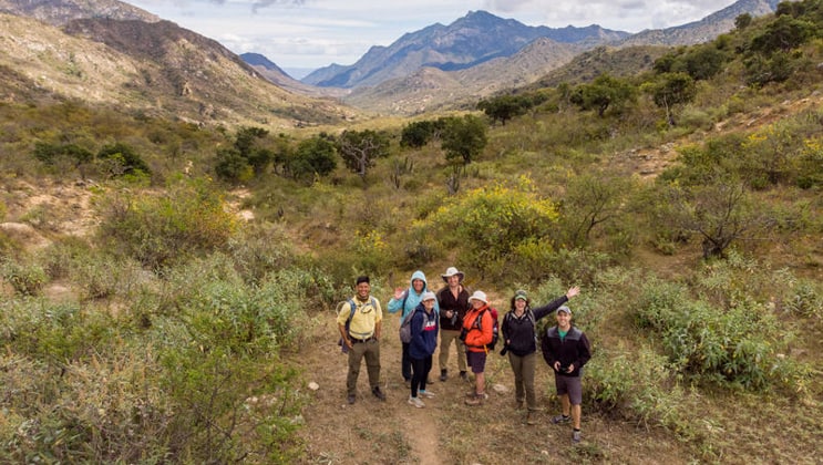 Group of hikers smile for a photo among rugged green & gold mountains on the Seas & Sierra: Glamping Baja California Sur land tour,