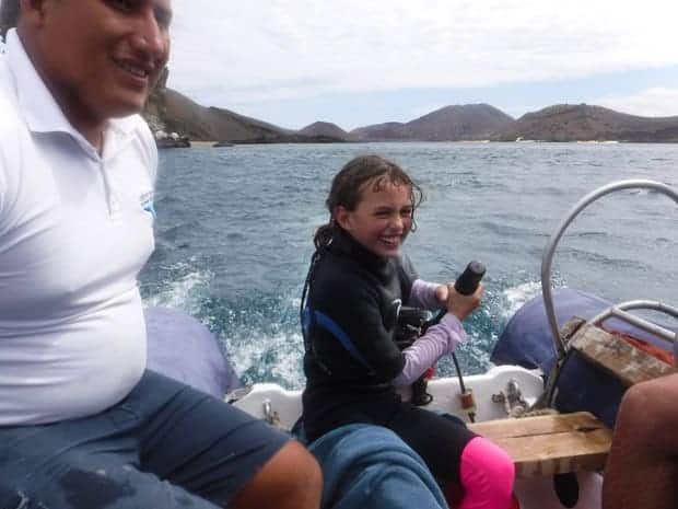 Happy child steer the skiff boat next to the guide from a small ship cruise in the Galapagos.