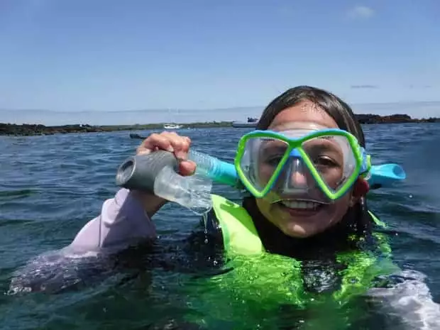 Child smiling with snorkel and mask on in the water on a small ship cruise snorkel tour. 