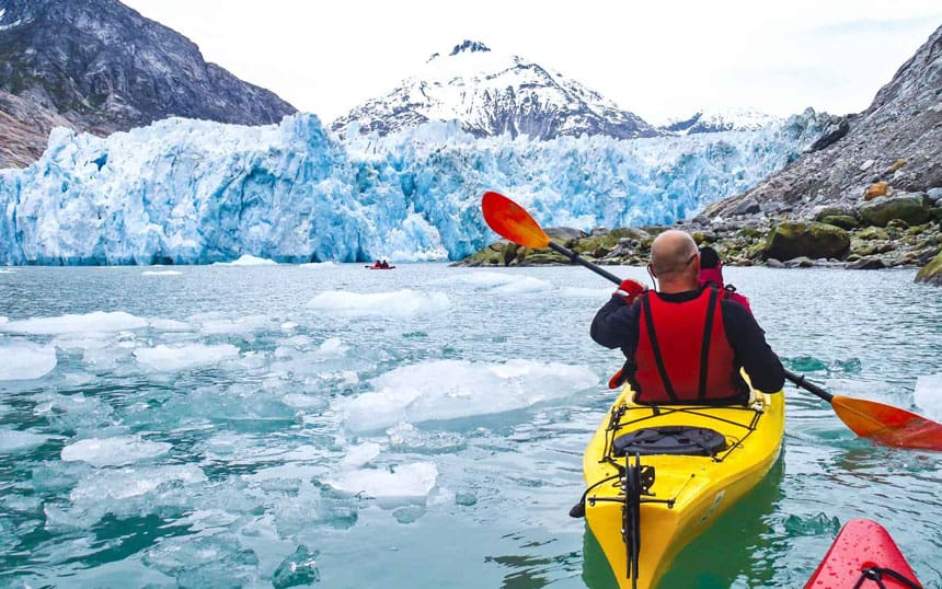 small ship cruise travelers kayaking in icy water in alaska with a glacier in the background