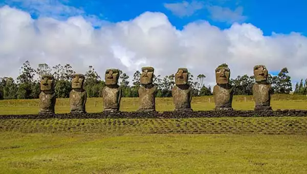 A line of moai stone statues with big heads, seen in a field of low-cut green grass on a sunny day during a trip to Chile.