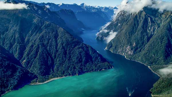 Aerial view of a New Zealand fjord in Fiordland National Park with clouds hovering over steep green hillsides