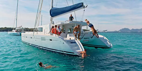Group of family travelers jump off the back of a private catamaran into calm turquoise waters during a Caribbean family vacation.