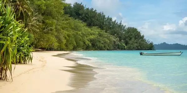 Small wooden dinghy sits anchored in calm turquoise waters by a deserted beach backed by lush jungle on a sunny day during a luxury Caribbean vacation.