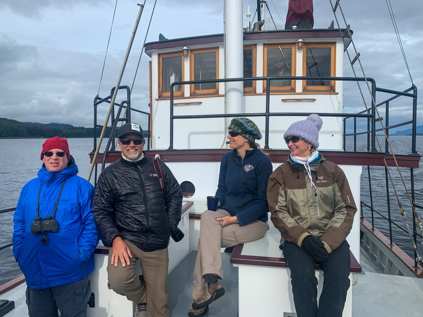 On a cloudy day, four cruise passengers sit on the deck of the small ship Catalyst as they cruise Alaska's inside passage
