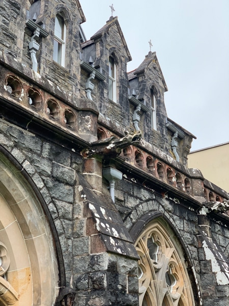 A close up of the stone work of a Scottish castle, gargoyle characters extend from columns in front of a wrap around terrace.