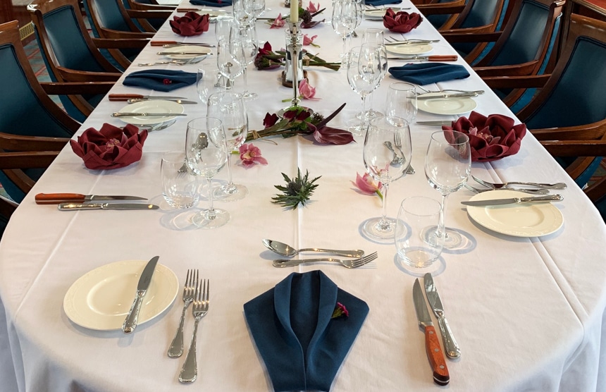 an empty dining table aboard Spirit of Scotland barge set with place setting and utensils, with a white table cloth and maroon napkins folded into the shape of a flower.