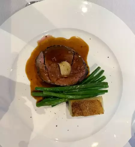 A dinner plate served aboard the Classic Scotland Barge Cruise, a piece of beef with potatoes, green beans and brown sauce overtop, sitting on a white plate.