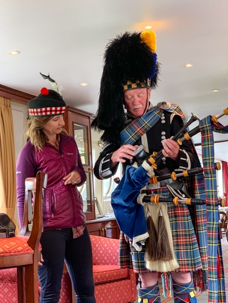 A local Scottish highlander dressed in traditional plaid garb holds a bagpipe as he shows the instrument to a female cruise guest the Spirit of Scotland barge